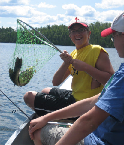 Max Winders' son, Tommy, proudly holding a fish he caught during a canoe trip in the Boundary Waters, displaying their catch with a big smile.