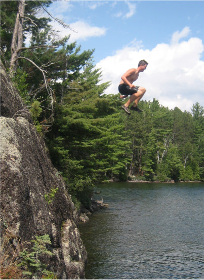 One of Max Winders' sons, Jeremy, mid-jump off a cliff into the lake, capturing the thrill of the adventure in the Boundary Waters.