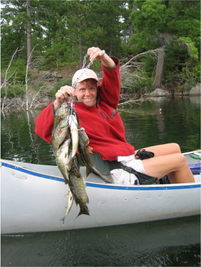 Karin, Max Winders' wife, proudly holding a string of fish she caught while canoeing in the Boundary Waters, smiling at her successful catch.